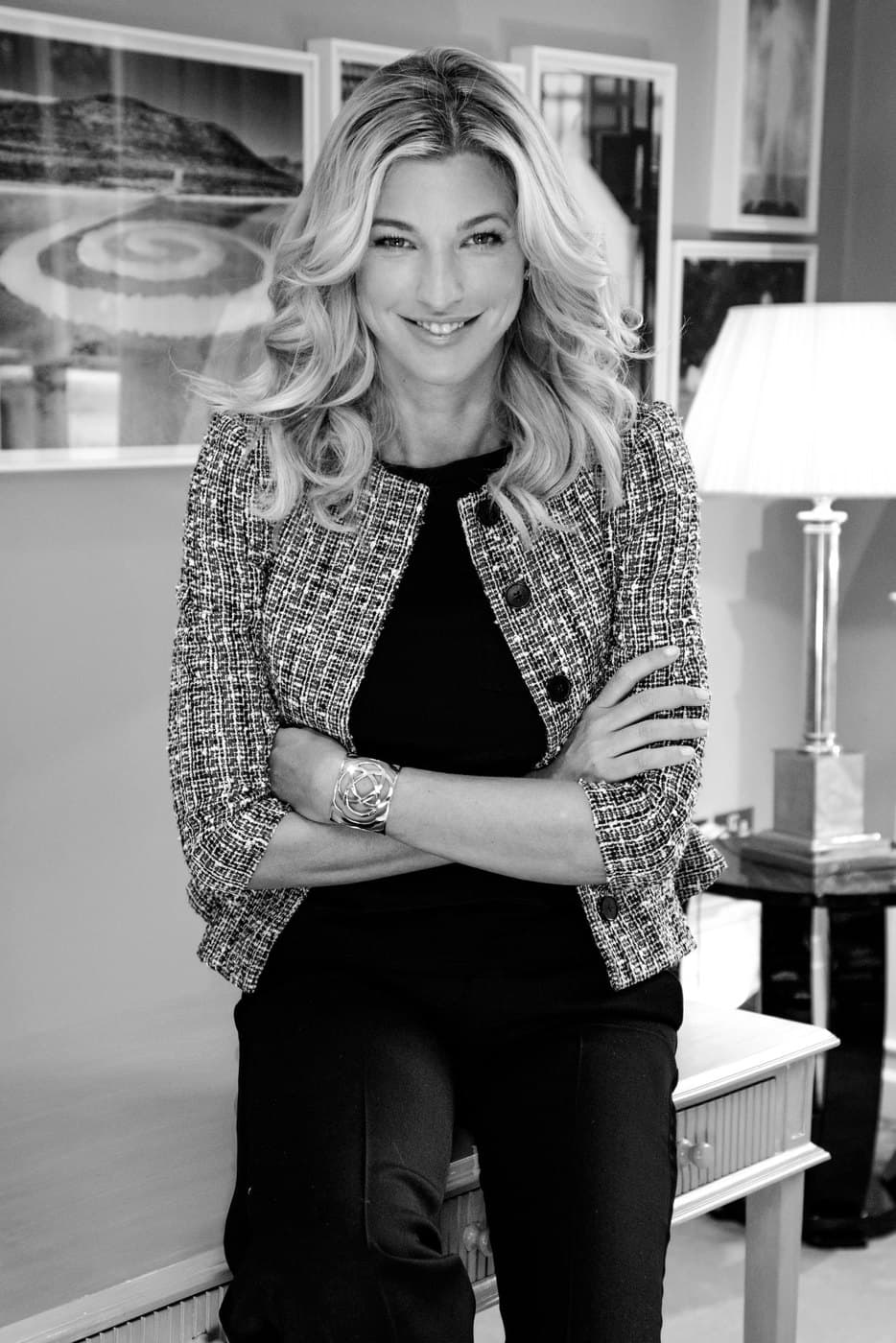 Black and white portrait of Nicole Junkermann in a tweed jacket, arms folded, in a room hung with framed pictures